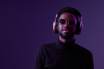 Obraz premium Confident young man wearing sunglasses and headphones, posing against a purple background, showcasing modern style and urban fashion, perfect for music and lifestyle themes
