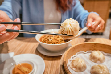 Close up of woman using chopsticks picking up a xiaolongbao dumpling from bamboo steamer basket in...