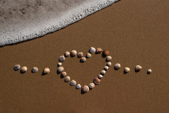 heart shape made out of seashells on the sand with a wave in the frame sea ocean beach coast love 