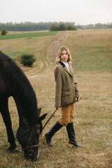 Woman in Equestrian Outfit Standing With Horse on a Scenic Meadow