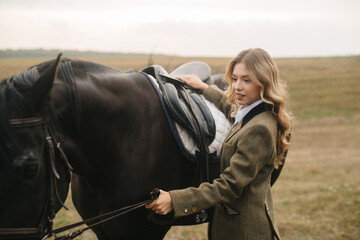 Obraz premium Elegant Woman Preparing a Horse for a Ride in a Field