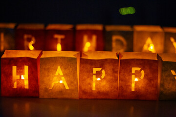 cardboard boxes illuminated with candles inside with letters cut out with the construction of the word happy birthday