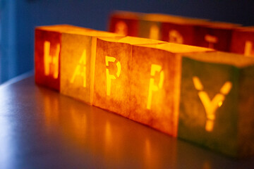 cardboard boxes illuminated with candles inside with letters cut out with the construction of the word happy birthday