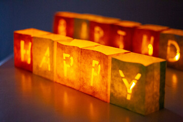 cardboard boxes illuminated with candles inside with letters cut out with the construction of the word happy birthday