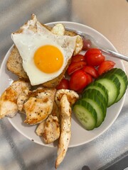 Hearty Breakfast Plate: A balanced and delicious breakfast featuring grilled chicken, a fried egg sunny-side up on whole-wheat toast, sliced cucumbers, and cherry tomatoes.