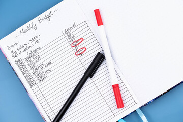Open daily planner notebook on desk, with neatly handwritten organized Monthly Budget tracking. With dates, categories and expenses. Personal finance management, spending and budgeting habits concept.