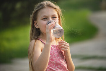 Portrait of a little girl drinking water from a reusable drinking bottle outside in the summer...