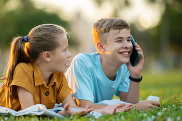 Sad teen friend being ignored by another outdoors while he is talking happily on mobile phone and...