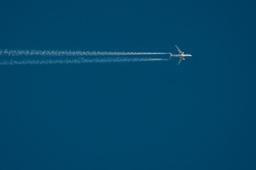 A high-altitude airplane soars through a deep blue sky, leaving behind two distinct contrails. The image captures the beauty of air travel and aviation dynamics. Copy space included.