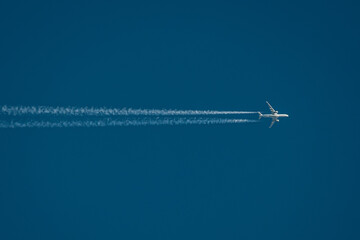 A high-altitude airplane soars through a deep blue sky, leaving behind two distinct contrails. The image captures the beauty of air travel and aviation dynamics. Copy space included.