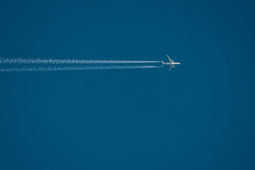 A high-altitude airplane soars through a deep blue sky, leaving behind two distinct contrails. The image captures the beauty of air travel and aviation dynamics. Copy space included.