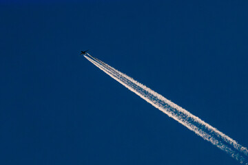 A high-altitude airplane soars through a deep blue sky, leaving behind two distinct contrails. The...