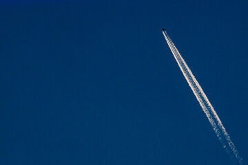 A high-altitude airplane soars through a deep blue sky, leaving behind two distinct contrails. The image captures the beauty of air travel and aviation dynamics. Copy space included.