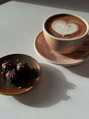 A cup of hot cocoa with a heart-shaped latte art design and chocolate truffles decorated with tiny hearts.
