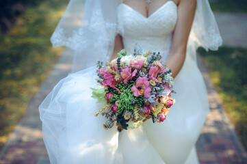Bride in a white wedding dress holding a vibrant bouquet with wildflowers, greenery, and rustic...