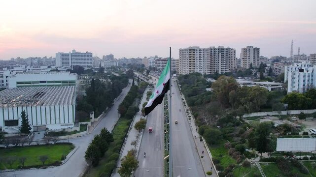 New Syrian Flag Waves on a Towering Pole in a Public Square. Syrian revolution against Bashar al-Assad.