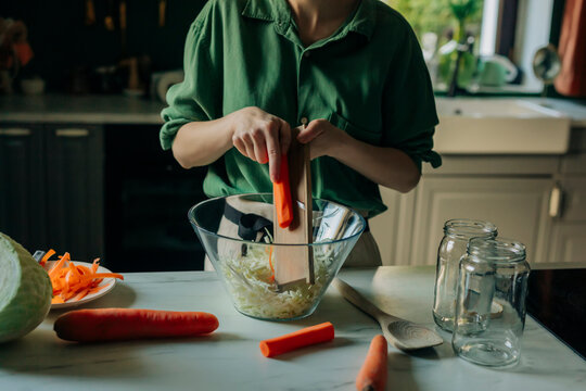 Mid adult woman preparing sauerkraut with cabbage and carrots in a home kitchen