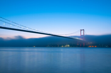 View of July 15 Martyrs Bridge (Bosphorus Bridge) with seagull and sunrise in fog clouds. Fishing boats in the foggy Bosphorus.
