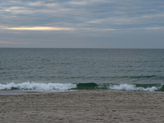 The photo captures a calm sea with small waves breaking on the sandy beach.