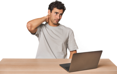 Hispanic young man working on laptop touching back of head, thinking and making a choice.