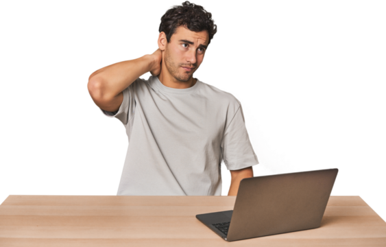 Hispanic young man working on laptop touching back of head, thinking and making a choice.