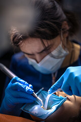 The dentist treats the child's tooth using a rubber dam. Close-up of tooth treatment.