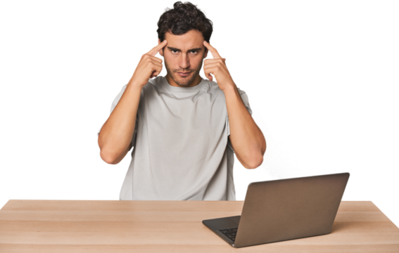 Hispanic young man working on laptop focused on a task, keeping forefingers pointing head.