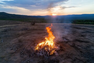 Fototapeta premium A small bonfire crackling at dusk on an open field, creating an atmospheric scene that emphasizes tranquility and the beauty of nature against a fading sky.