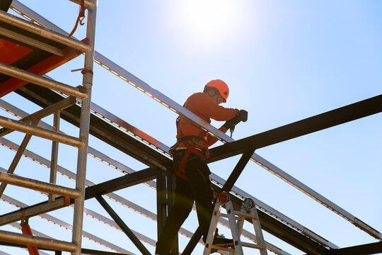 Construction worker using drill machine on metal scaffold under sky