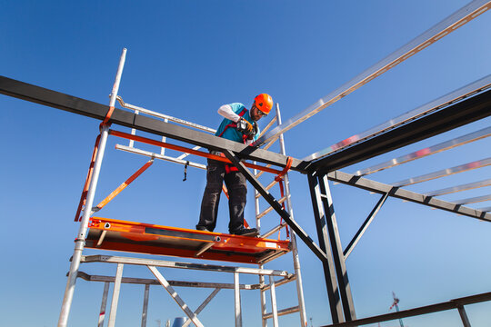 Mature construction worker installing metal tubes with drill under blue sky