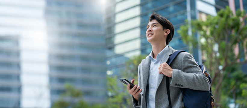 smiling happy successful asian businessman or lawyer in gray suit and blue shirt calling with his phone near his ear standing in front of an office building.Successful businessman holding mobile phone