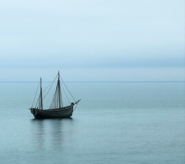Fototapeta premium Solitary Vessel Drifting on Calm Waters Under a Pale Sky An Image of Tranquility and Reflection