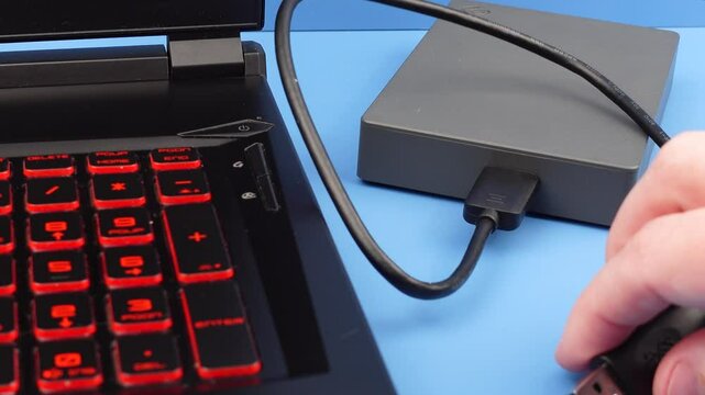 External hard drive HDD connected to a laptop via USB cable for data backup and storage. Concept of data security, file management, digital organization, and preventing data loss. 