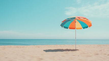 A colorful beach umbrella standing tall on a sandy beach, with clear blue skies and the ocean in the background, perfect for a summer vibe