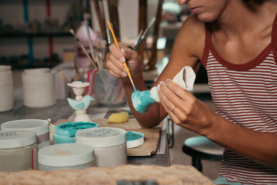 Close-up of a woman sitting a table in a pottery studio glazing a candlestick