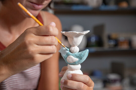 Close-up of a woman sitting at a table in a pottery studio glazing a clay candlestick