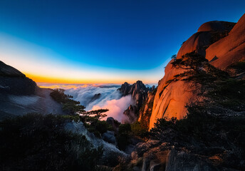 Obraz premium Breathtaking China landscape at sunset. Mountain peaks rise above a sea of clouds in the valley. Orange and blue sky creates a scenic vista.