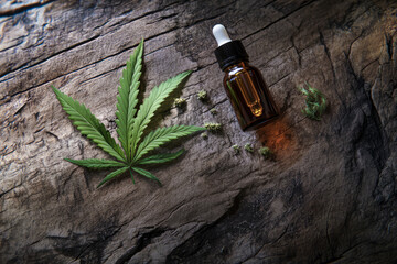 A cannabis leaf, buds, and an amber dropper bottle arranged on a textured wooden surface, bathed in natural light with earthy tones
