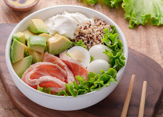 Salmon quinoa bowl with greens and vegetable on the wooden table. Balance in bowl. Top view.