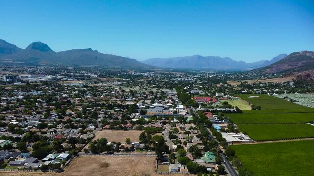 Camera moving up along the main road leading into Paarl Town South Africa with the iconic Paarl rock and the Mountain range behind the town 4K Aerial Video