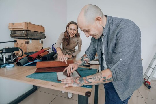 Happy businesswoman discussing with businessman measuring leather patch at workbench