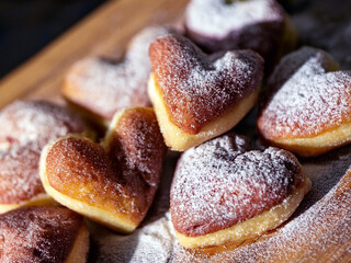 Heart-shaped mini donuts with powdered sugar on parchment paper, showcasing a warm golden brown tones, ideal for Valentine's Day or romantic occasions.
