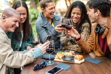 Multiracial people having fun drinking red wine out side at city winery bar - Happy friends sharing fancy time together at open air restaurant garden - Food and beverage and youth life style concept