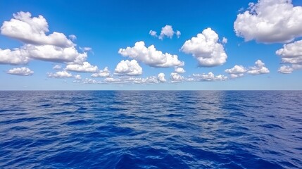 Obraz premium Wide shot of a calm water surface under a partly cloudy blue sky. The water is a deep blue with small waves creating subtle patterns. The sky has