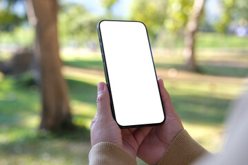 Mockup image of a woman holding mobile phone with blank white desktop screen in the outdoors