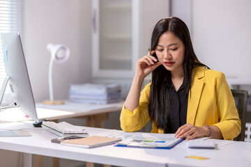 Fototapeta premium A woman in a yellow jacket is talking on her cell phone while sitting at a desk