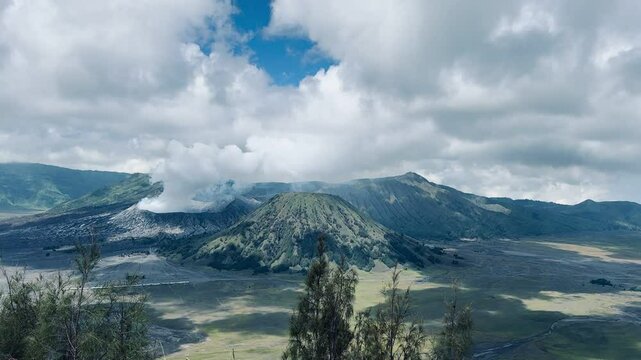 Aerial view of Mount Bromo and Mount Batok with white volcanic smoke rising over the vast sand sea in Indonesia. A stunning volcanic landscape in Bromo Tengger Semeru National Park.