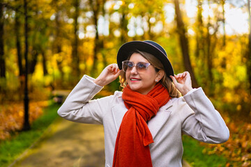 Portrait of beautiful middle aged woman in black brimmed hat and sunglasses standing in city park...