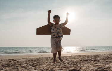 Happy boy with toy cardboard airplane play and jumping on the beach. Child enjoy on vacation creativity lifestyle of kid.