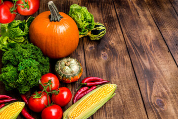 A vibrant autumn harvest arrangement featuring pumpkins, corn, chili peppers, tomatoes, and fresh greens on a rustic wooden background. Perfect for seasonal culinary inspiration.